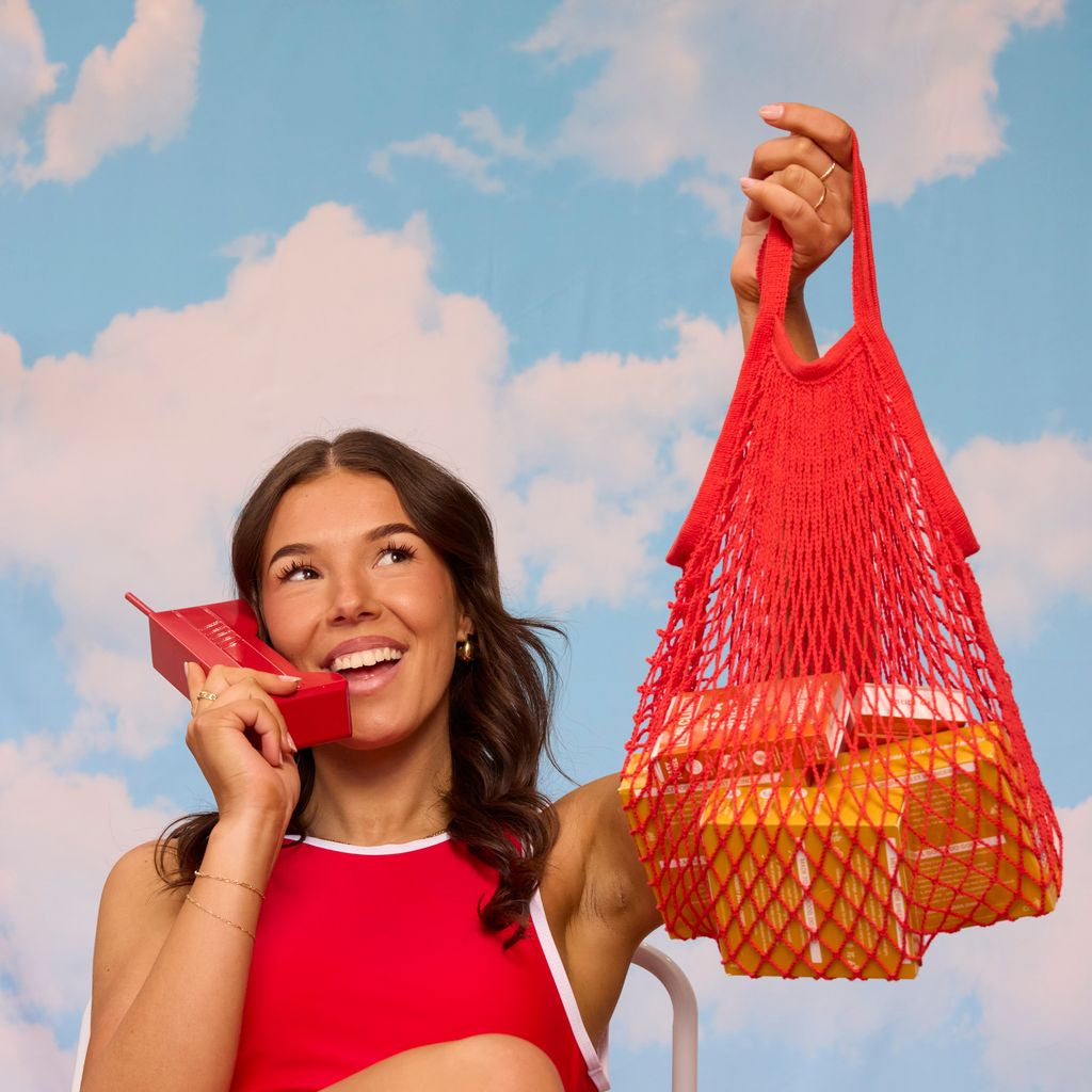 Woman in a red swimsuit holding a red bag against a blue sky with clouds background